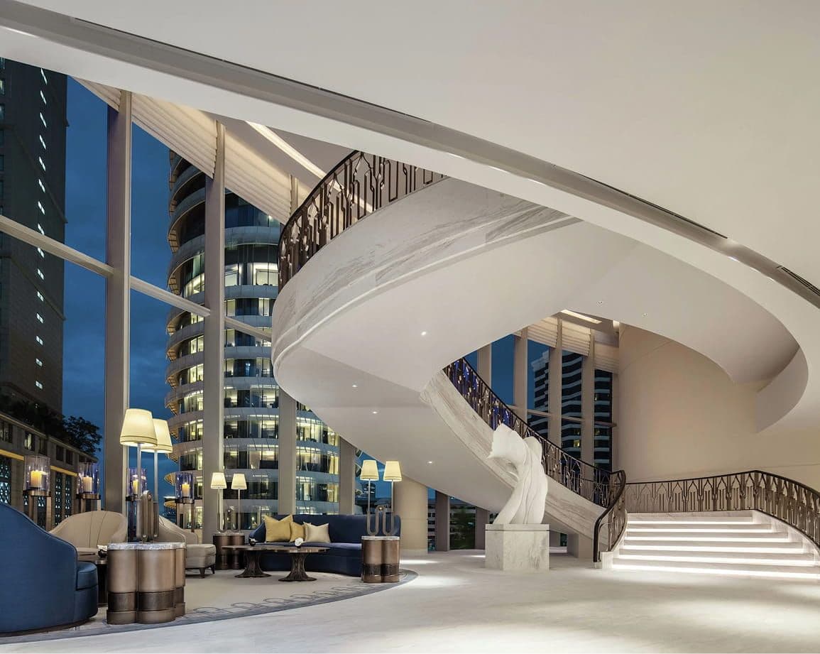 Luxurious hotel lobby with a grand spiral staircase and panoramic city views at night.