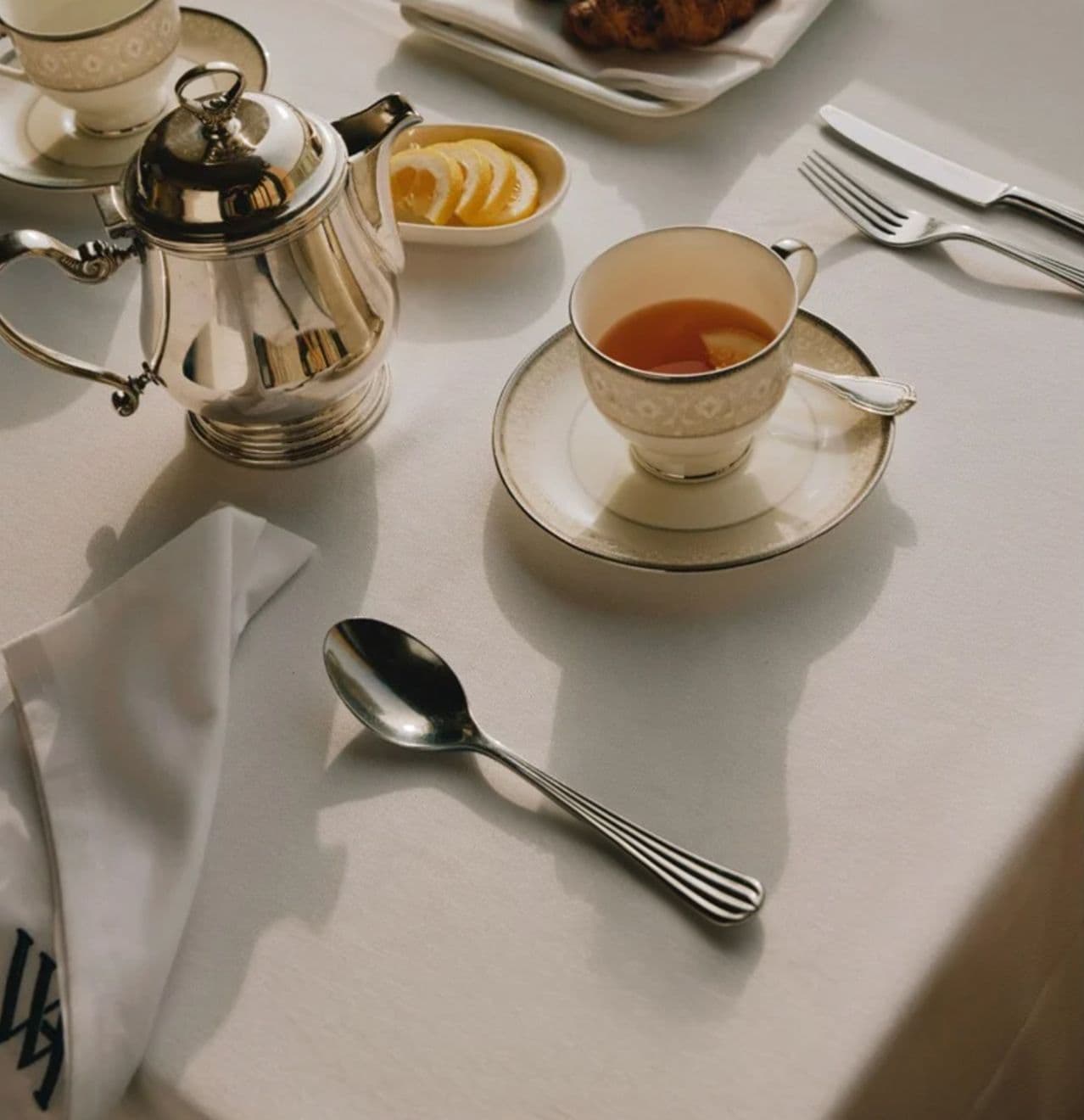 Elegant silver teapot, teacup, and spoon on a white table with butter dish.
