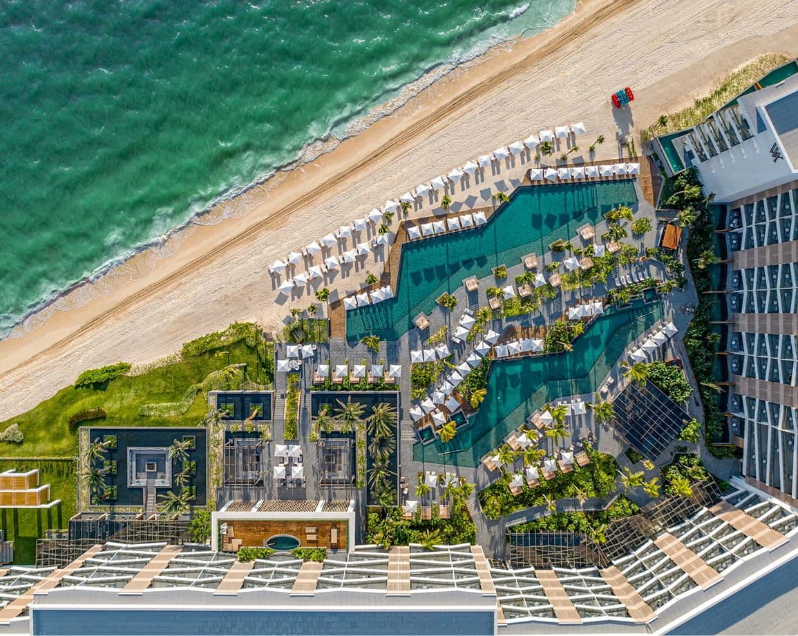 Aerial view: Luxury resort complex, multiple pools, sun loungers, golden beach, and turquoise ocean.