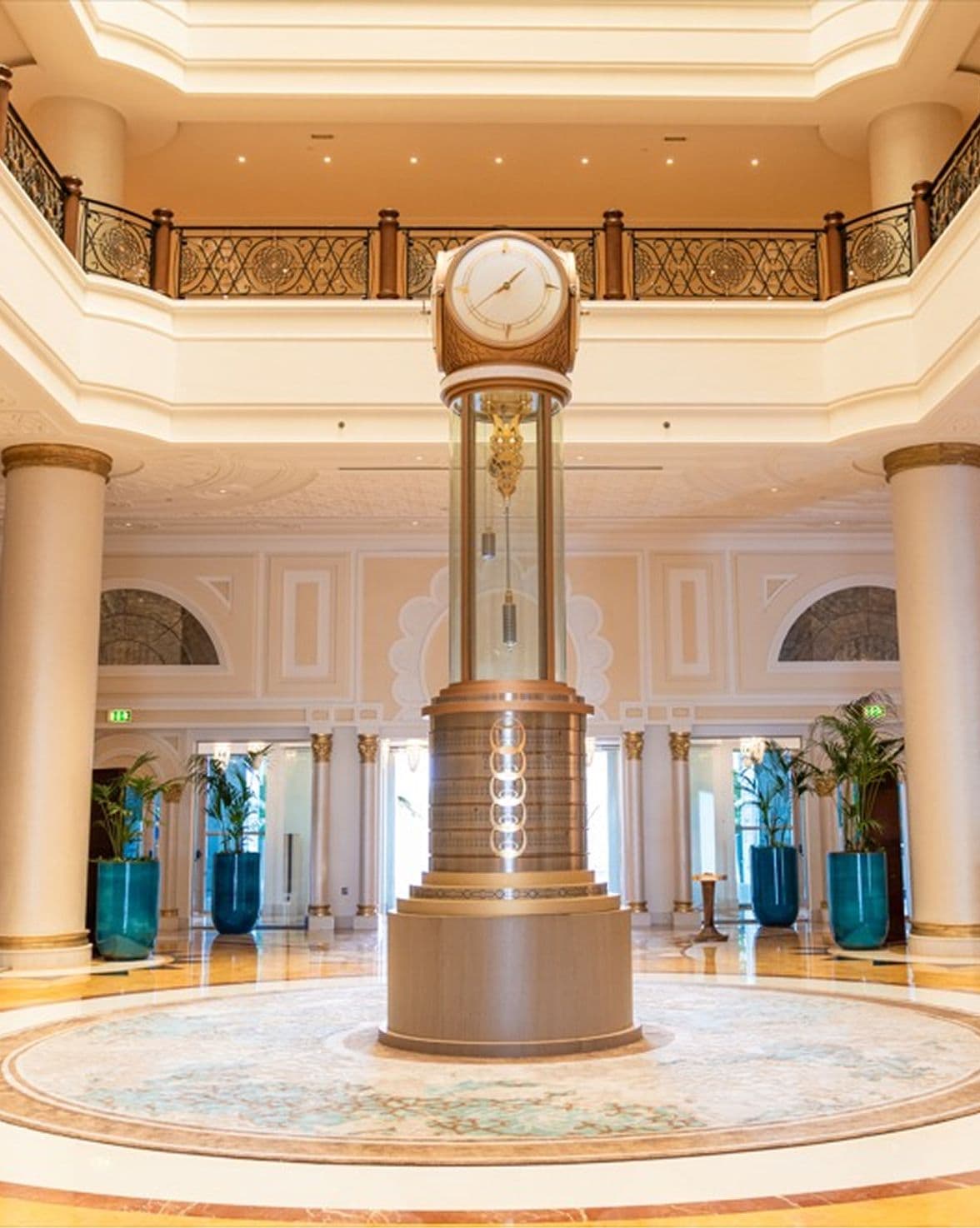 Ornate gold grandfather clock stands prominently in a luxurious hotel lobby with high ceilings.