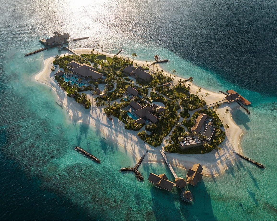 Aerial view of a luxury tropical island resort with white sand beaches and overwater villas.